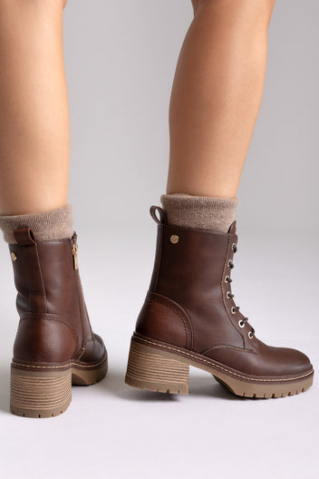 Model legs in brown leather lace-up ankle boots with chunky block heels and cuffed socks, angled view on a light backdrop
