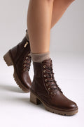 Model legs in brown leather lace-up ankle boots with chunky block heels and cuffed socks, angled view on a light backdrop