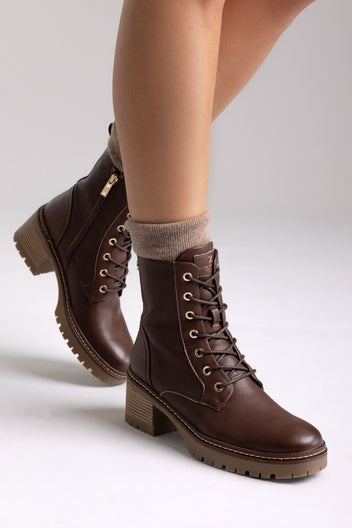 Model legs in brown leather lace-up ankle boots with chunky block heels and cuffed socks, angled view on a light backdrop