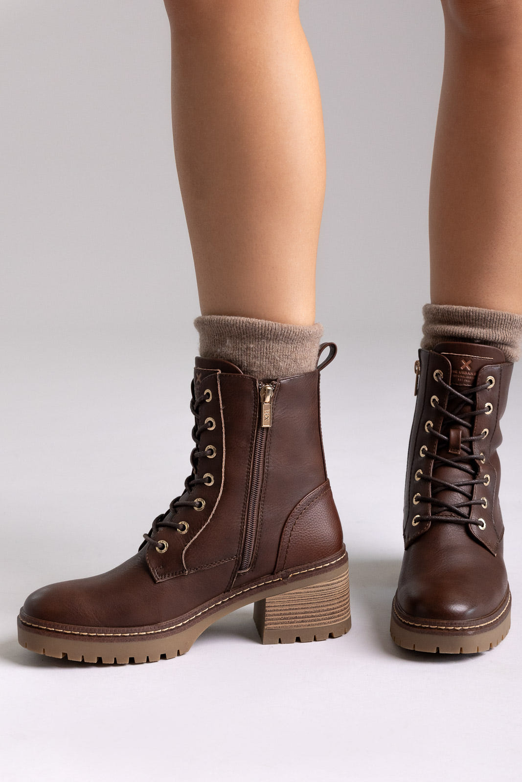 Model legs in tan leather lace up combat boots with sock cuff and block heel, front view on light grey background