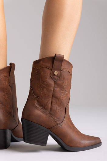 Brown leather western ankle boots with block heel and pointed toe, angled view on a model in studio light