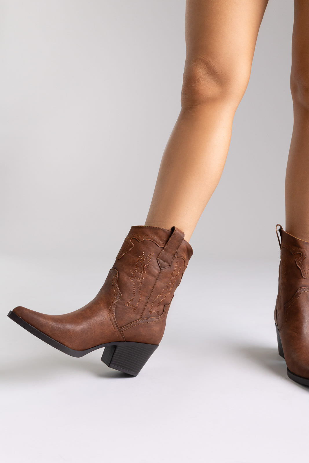Brown leather western ankle boots with stitched detail and block heel, angled view on a model in studio light