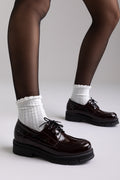 Model legs in burgundy patent chunky sole lace up shoes with white socks, front view on light grey background