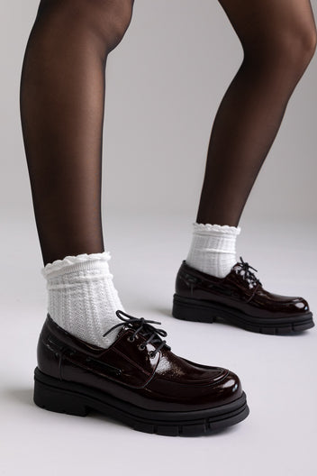 Model legs in burgundy patent chunky sole lace up shoes with white socks, front view on light grey background