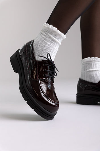 Model legs in burgundy patent chunky sole lace up shoes with white socks, angled view on light grey background