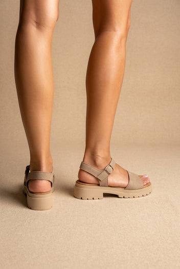 Rear and side view of beige suede sandals with a wide front strap, buckled ankle strap and a chunky cream lugged sole, on a model