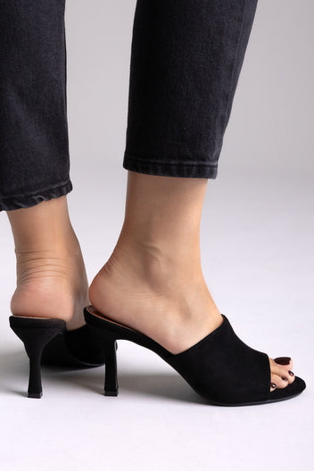 Black suede pointed-toe kitten-heel mules with open toe, side view on a model in black jeans