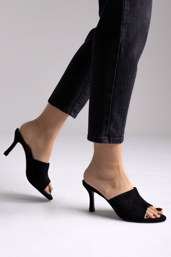 Black suede peep-toe kitten-heel mules, angled view on a model in black jeans in studio light