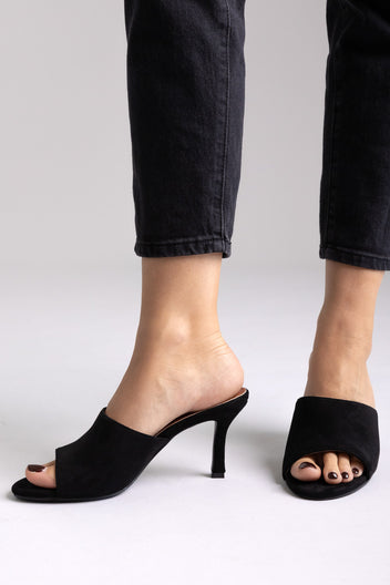 Black suede open-toe kitten-heel mules, side view on a model in black jeans in studio light