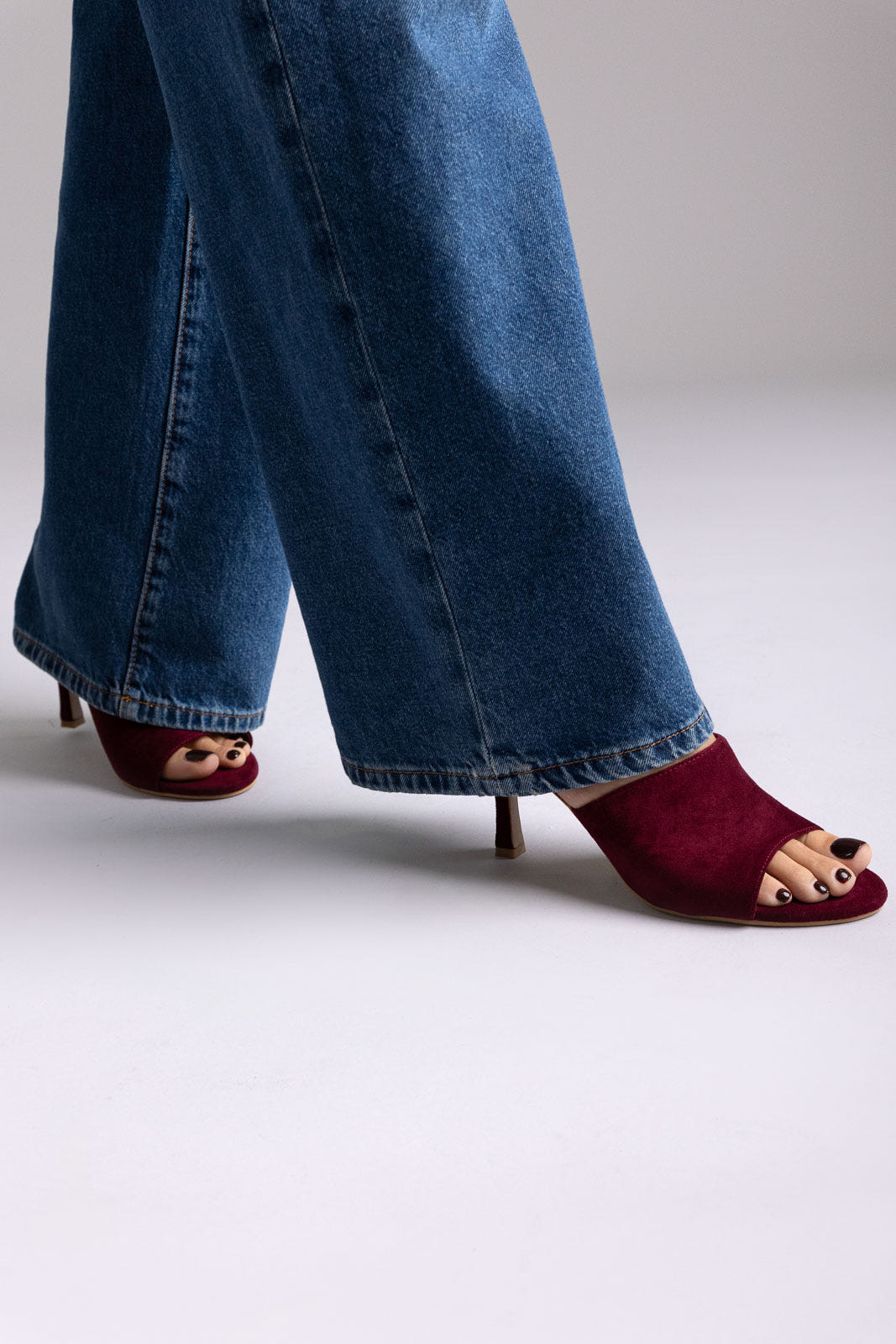 Burgundy suede open-toe kitten-heel mules, angled view on a model in jeans in studio light