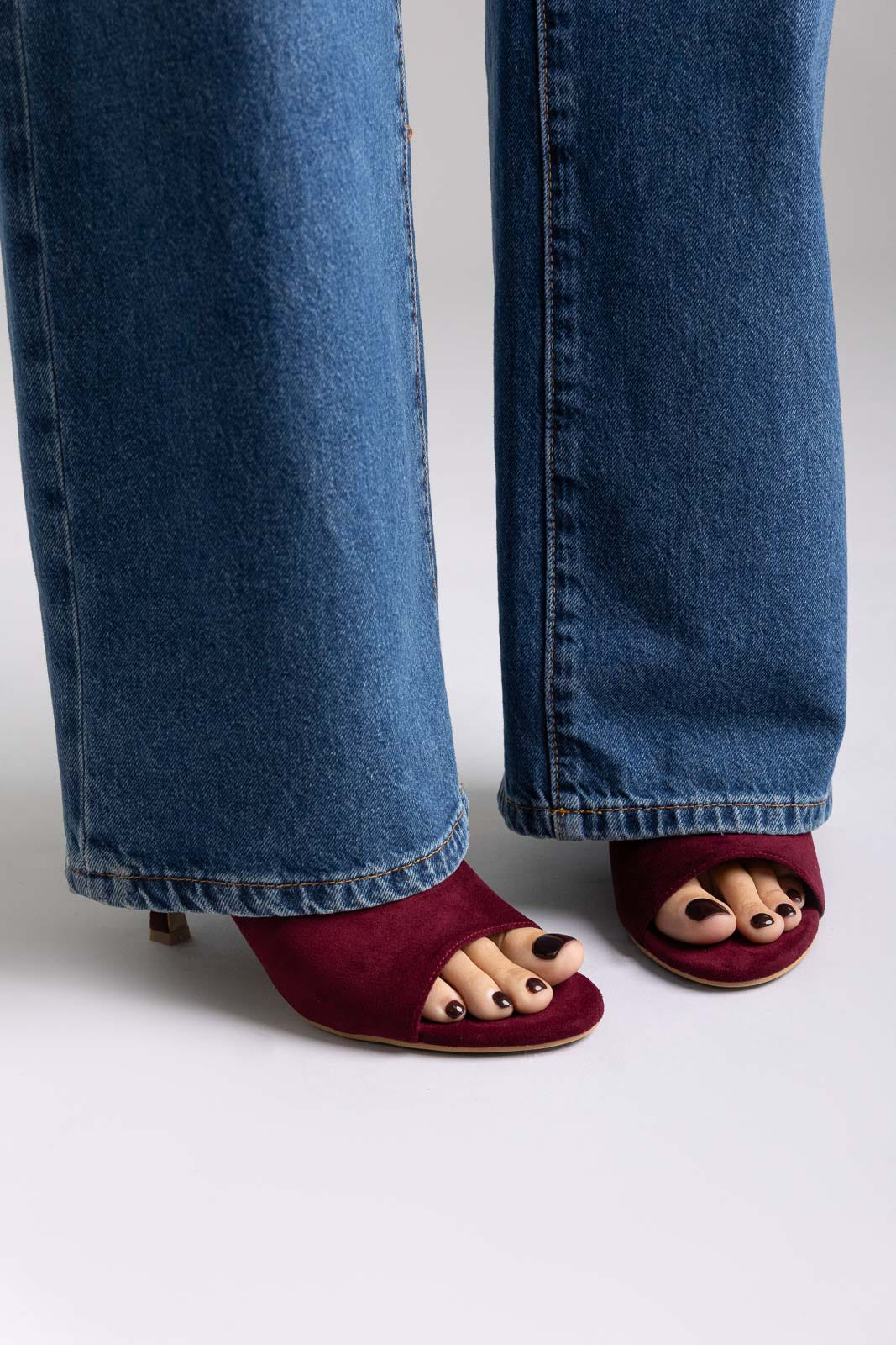 Burgundy suede open-toe kitten-heel mules, front view on a model in jeans in studio light