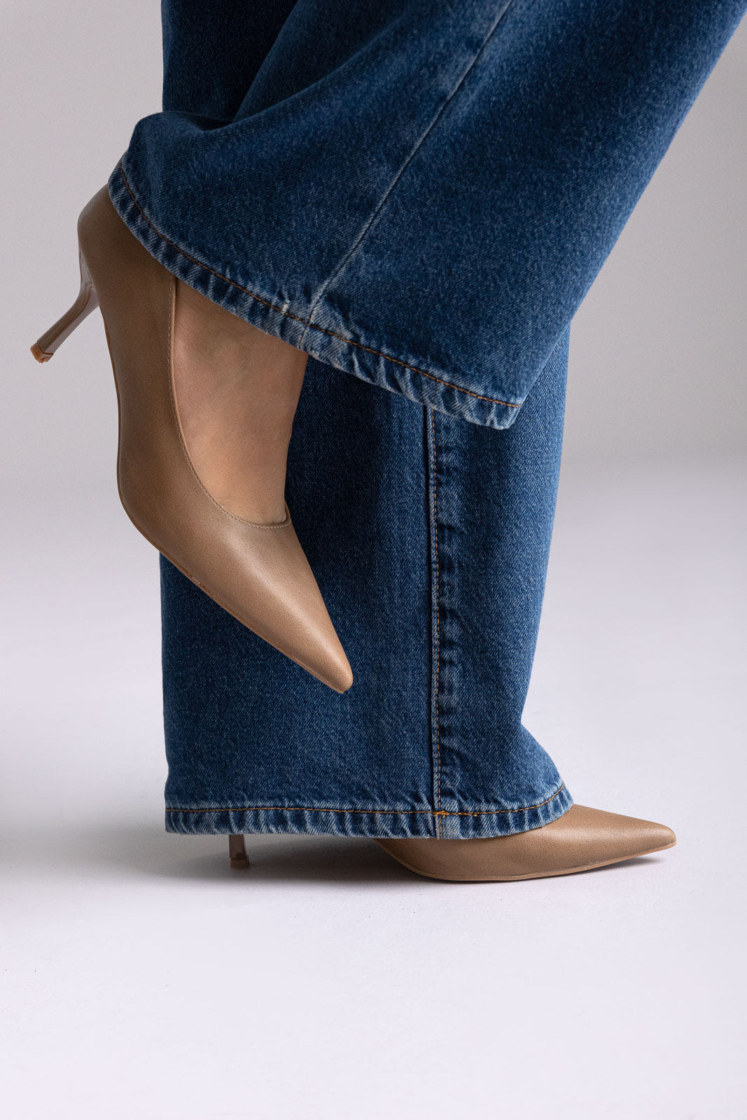 Tan leather pointed-toe kitten-heel pumps, angled view on a model in wide-leg jeans