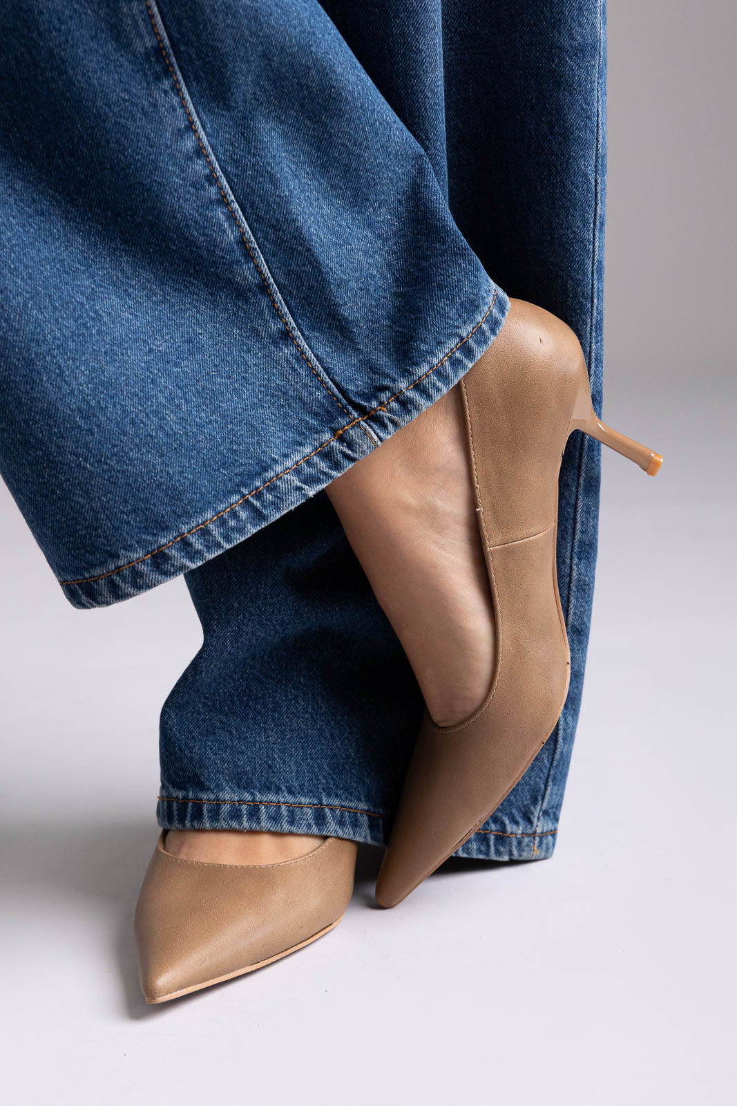 Tan leather pointed-toe kitten-heel pumps, angled view on a model in wide-leg jeans