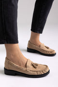 Taupe suede tassel loafers with rubber sole, angled view on a model in black jeans