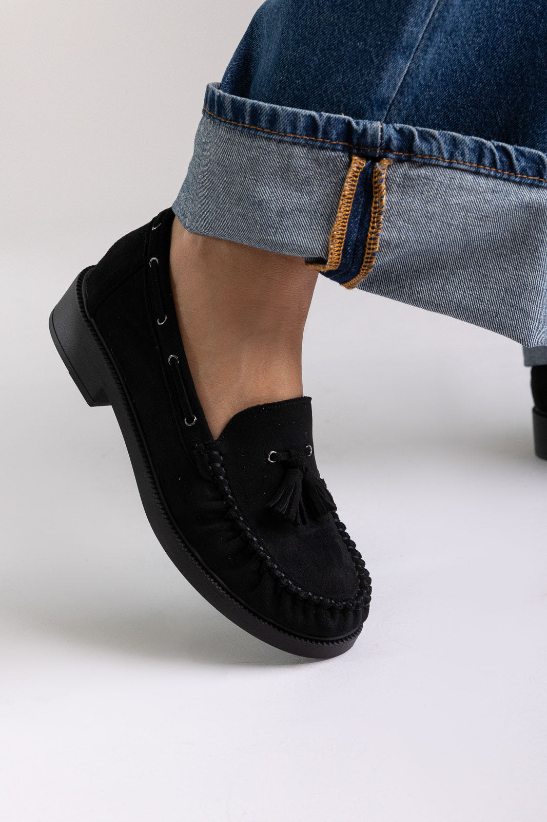 Black suede loafers with chunky sole, angled view on a model in cuffed jeans in studio light