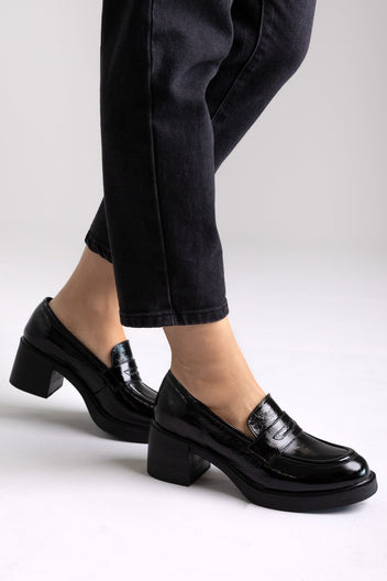 Black patent leather penny loafers with block heel and chunky sole, side view on a model in black jeans
