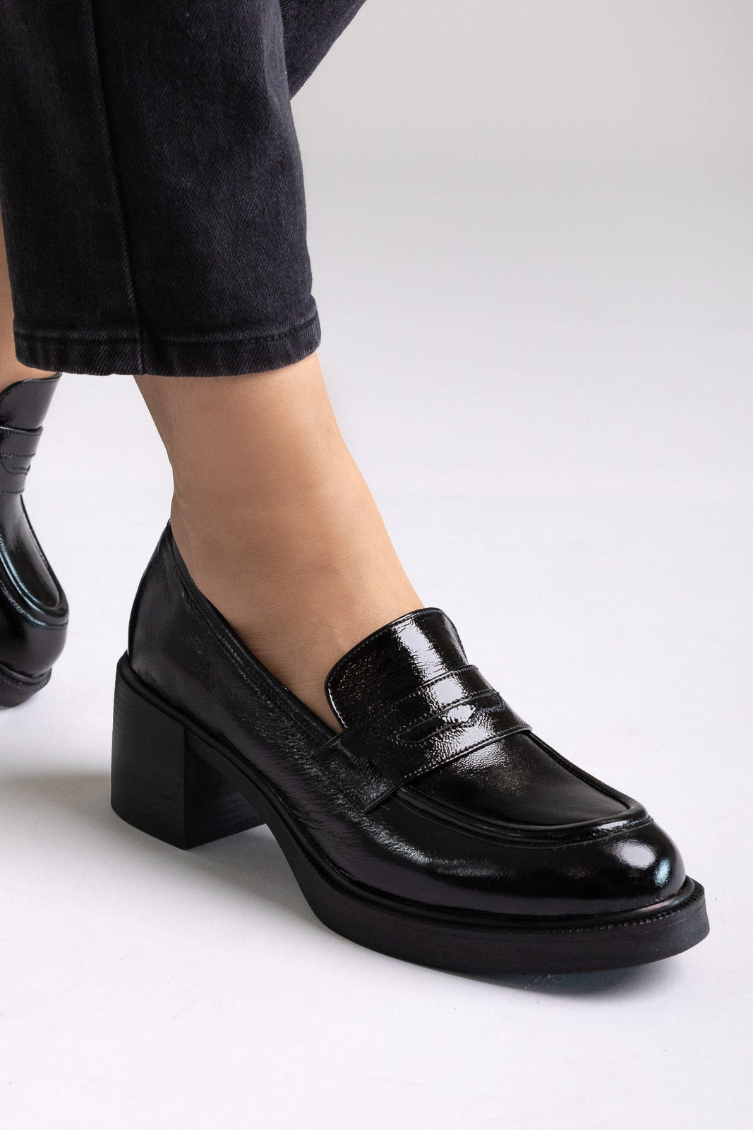 Black patent leather penny loafers with block heel and chunky sole, angled view on a model in black jeans