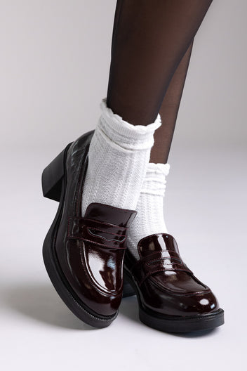 Oxblood patent leather penny loafers with block heel, angled view on a model with white socks and tights