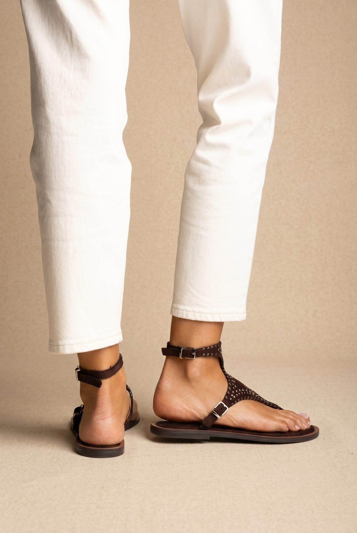 Dark brown studded suede thong sandals with buckled ankle straps on a flat sole, back and side view worn on a model