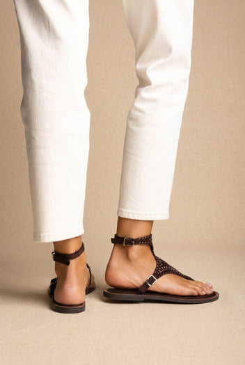 Dark brown studded suede thong sandals with buckled ankle straps on a flat sole, back and side view worn on a model