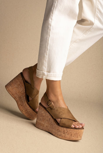 Tan suede crossover-strap sandals with a chunky cork platform wedge and buckled ankle strap, three-quarter view worn on a model