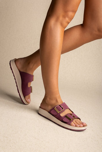 Mauve two-strap buckle slides with gold buckles and a cream platform sole, three-quarter view on a model