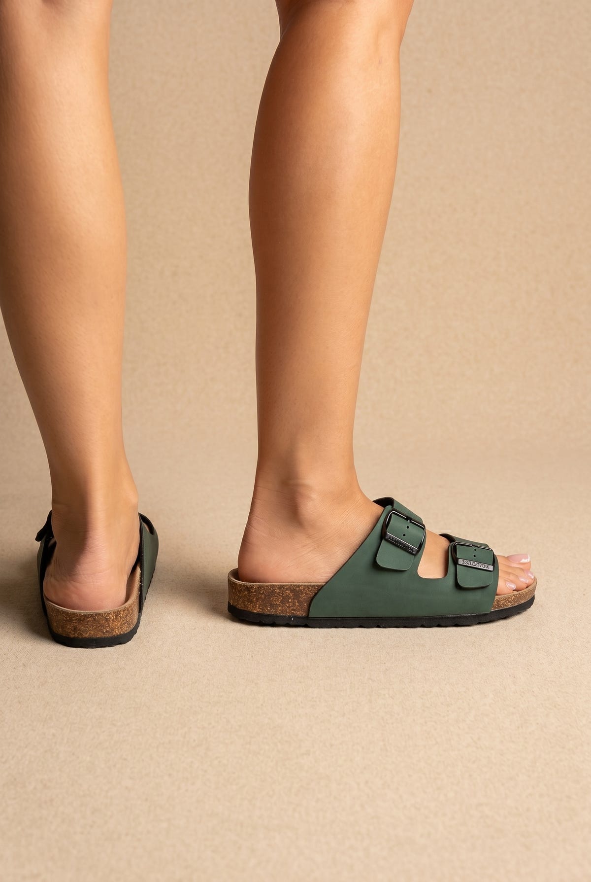 Green two-strap slides with black buckles, cork footbed and black sole, back and side view on a model