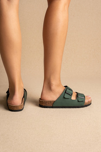 Green two-strap slides with black buckles, cork footbed and black sole, back and side view on a model