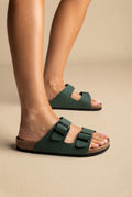 Green two-strap buckle slides with cork footbed and black sole, three-quarter side view on a model