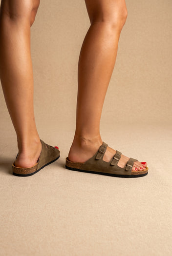 Olive brown suede three-strap buckle sandals with cork footbed and black sole, side view worn on a model
