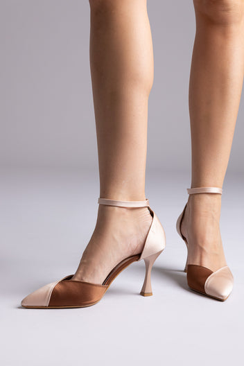 Blush pink and caramel brown pointed ankle-strap pumps with flared heels, worn by a model in front view