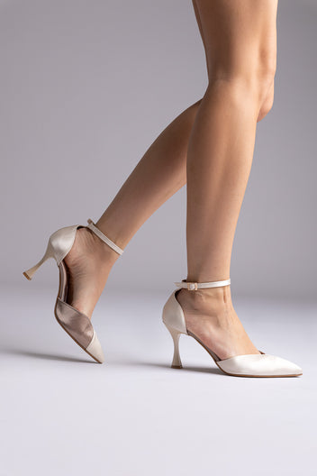 Ivory satin pointed ankle-strap pumps with flared heels and thin buckled straps, worn by a model with one foot raised