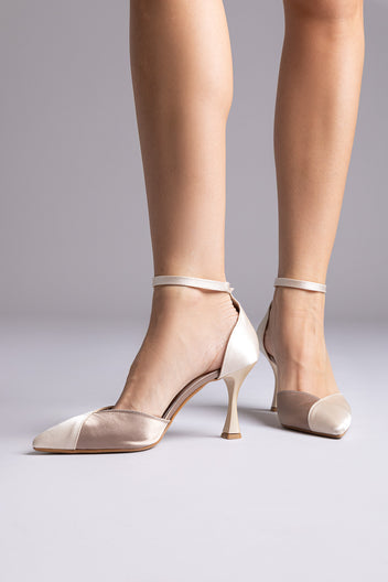 Ivory and champagne satin pointed ankle-strap pumps with flared heels and thin straps, worn by a model, front view