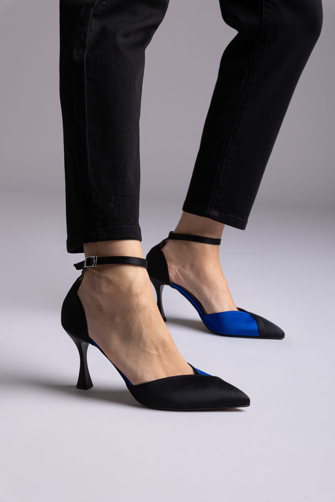 Black satin d'Orsay pumps with royal blue inner panels, ankle strap and flared heel, worn with black jeans