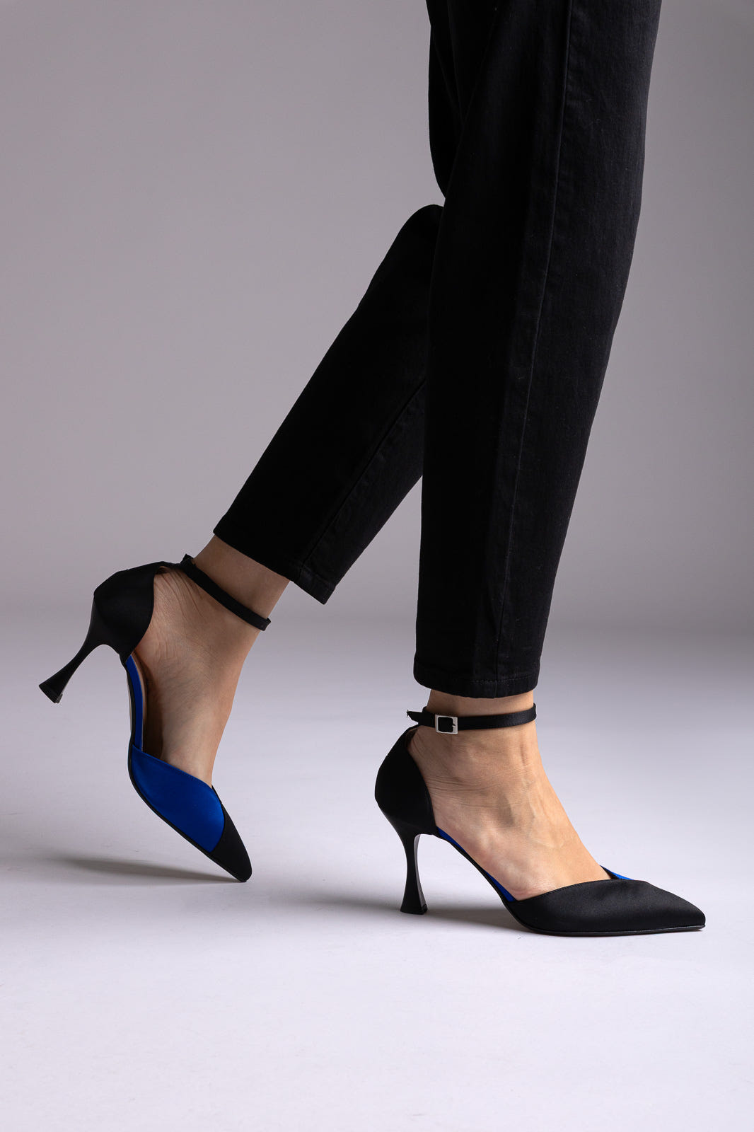 Black satin pointed pumps with cobalt blue inner side, ankle strap and flared heel, worn with black skinny jeans