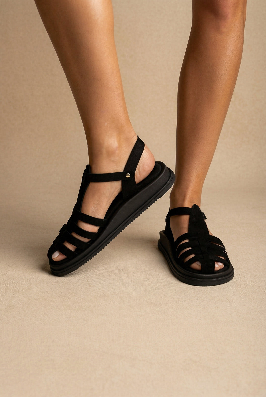 Black suede fisherman sandals with woven cage straps, ankle strap and chunky sole, three-quarter view on a model