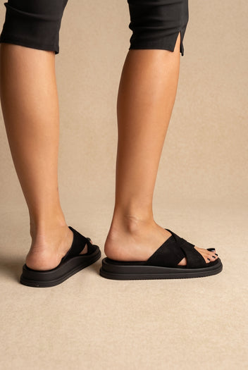 Black suede crossover-strap slides with chunky black platform sole, back and side view on a model