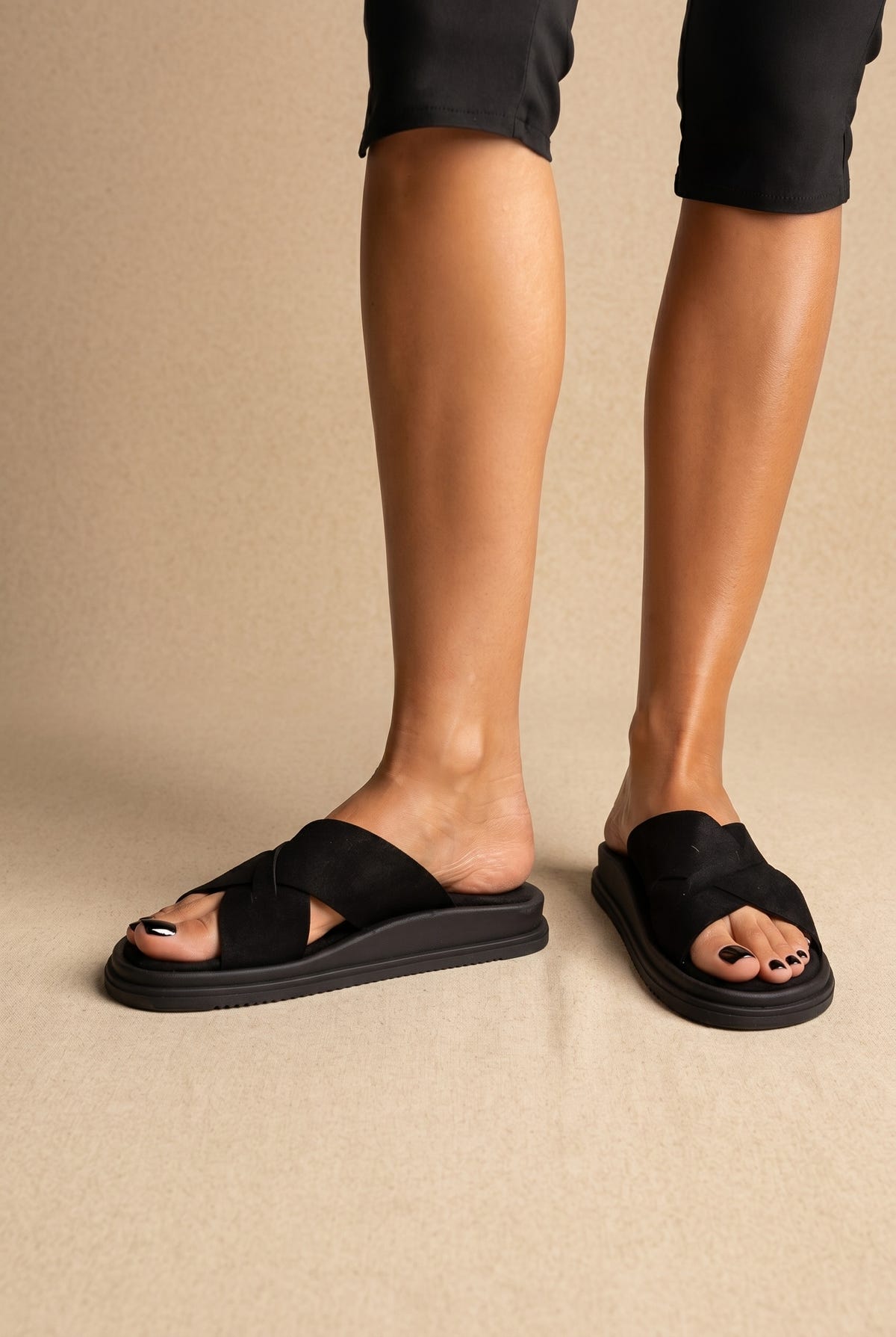 Black crossover-strap slides with thick black platform sole, front view worn on a model