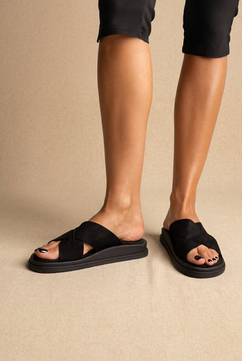 Black crossover-strap slides with thick black platform sole, front view worn on a model