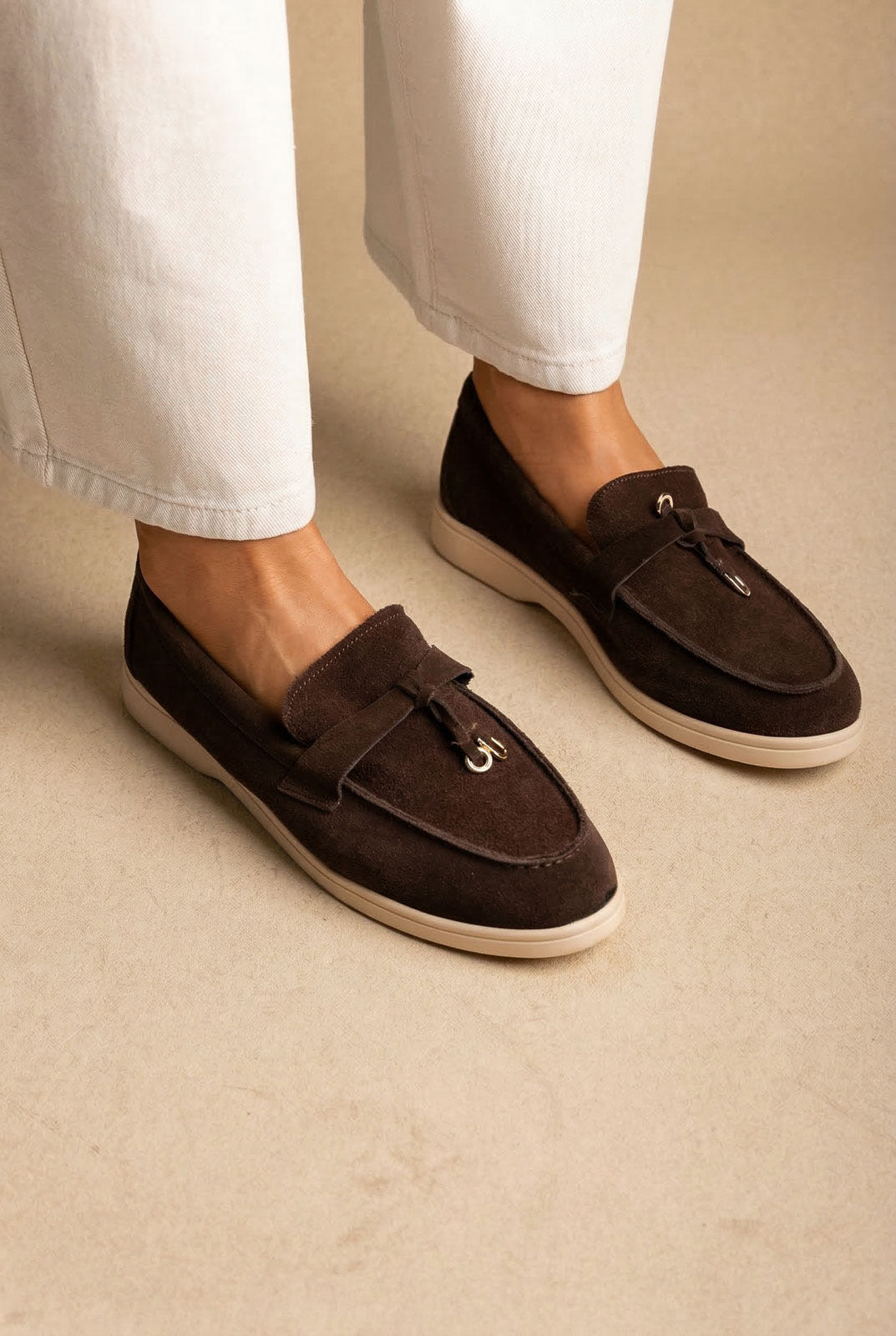 Model wearing dark chocolate suede loafers with knotted tie, gold ring detail and cream soles