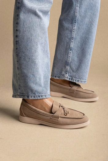 Model wearing taupe suede loafers with knotted tie, gold ring detail and cream sole, with light jeans