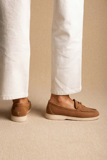 Back view of tan suede loafers with cream soles and tassel detail, worn with white wide-leg jeans