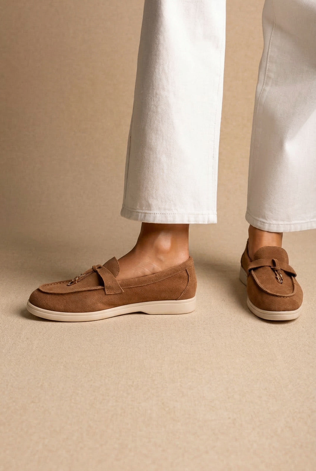 Model wearing tan suede loafers with leather tie detail and a cream sole, with white wide-leg jeans