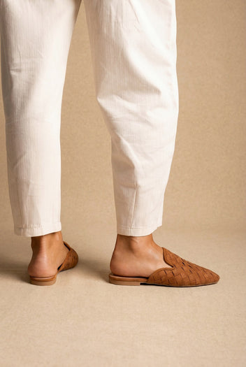 Back view of tan woven suede flat mules with pointed toe, worn with cream tapered trousers