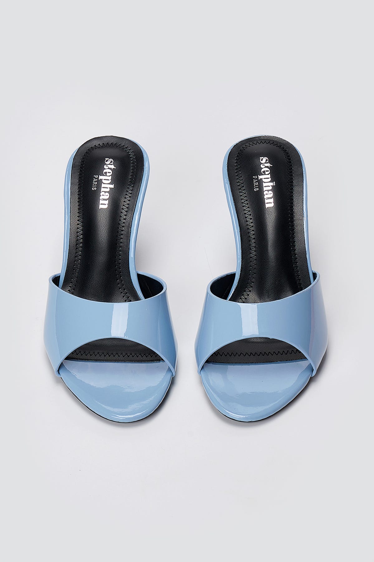 Pair of light blue patent leather heeled mules with open toes and black insoles, top-down view