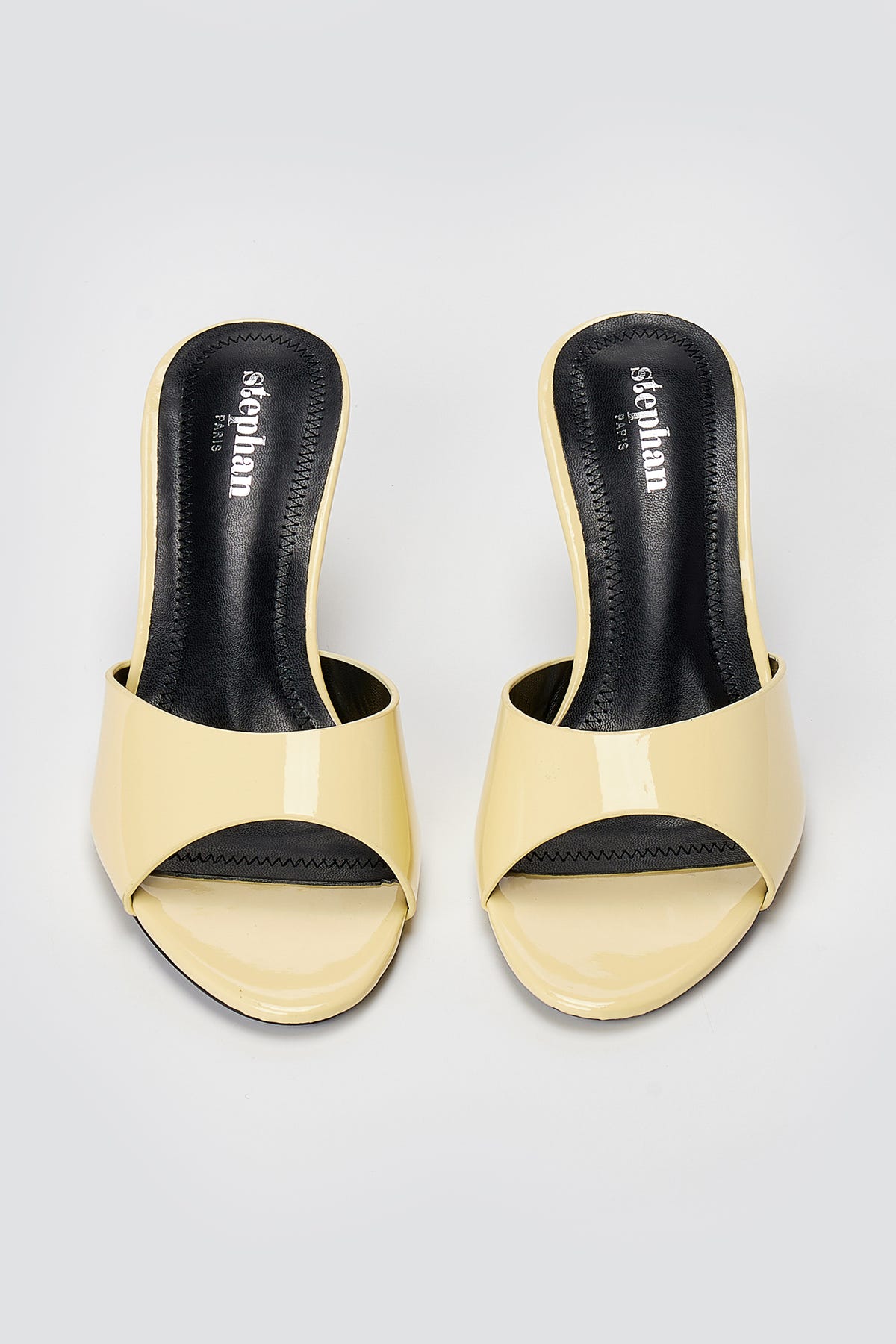 Pair of pale yellow patent leather heeled mules with open toes and black insoles, top-down view