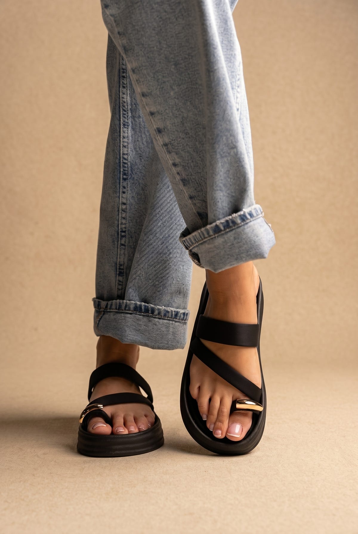 Black chunky flatform sandals with crossed straps and gold buckle details, worn with cuffed jeans, front view