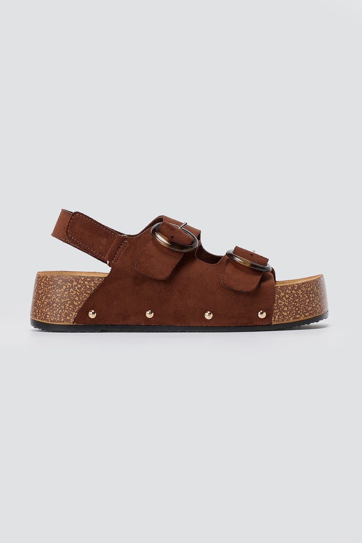 Brown suede platform sandal with two round buckles, slingback strap, gold studs and cork-style sole, side view