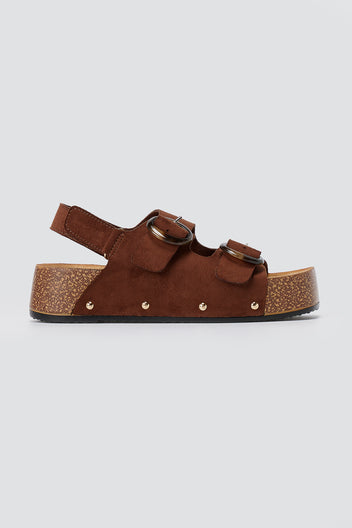 Brown suede platform sandal with two round buckles, slingback strap, gold studs and cork-style sole, side view