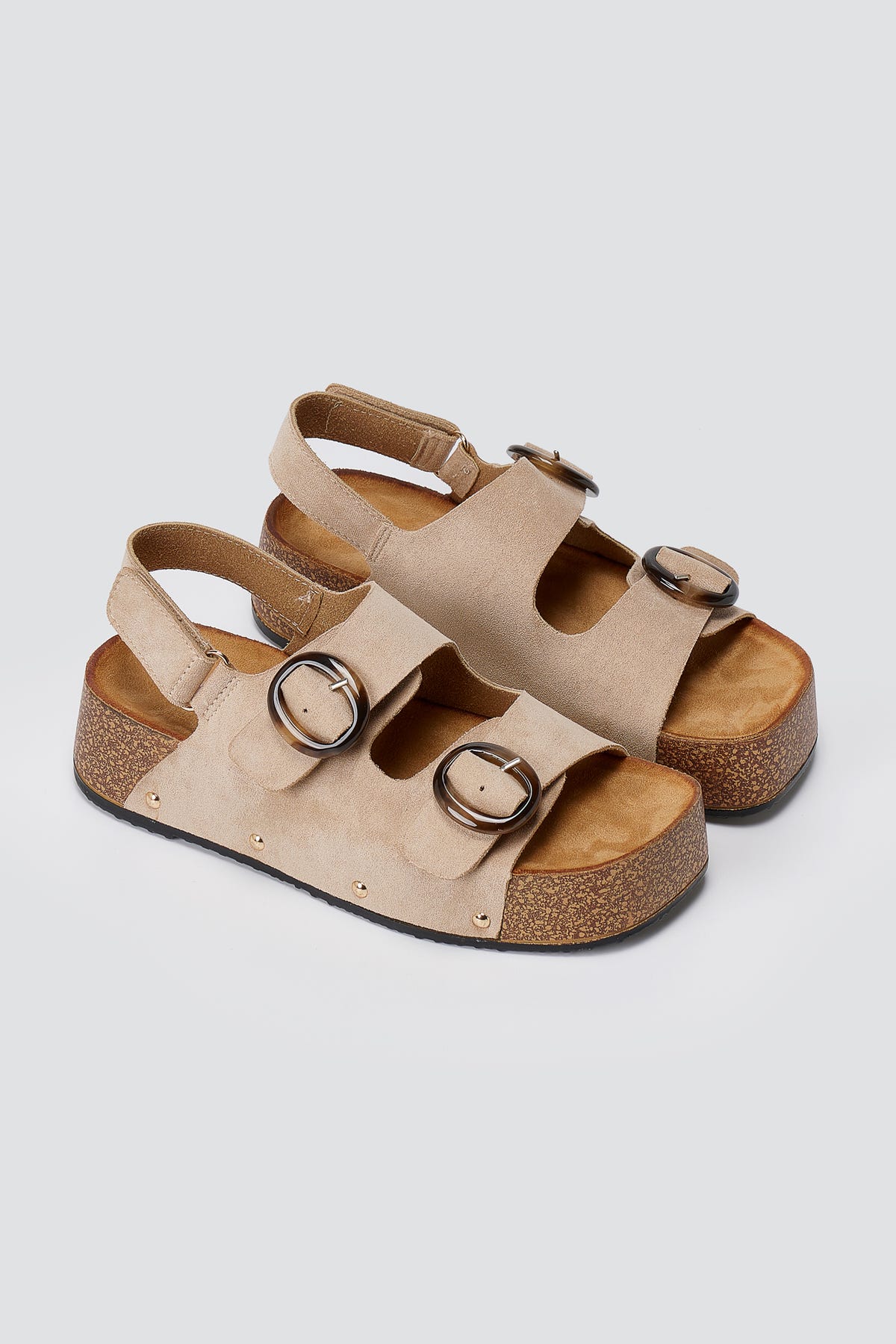 Pair of beige suede platform sandals with two round buckles, slingback straps and cork-style soles, three-quarter view